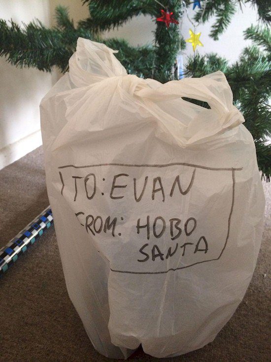 Present wrapped in a white plastic carrier bag labelled From Hobo Santa, under a Christmas tree