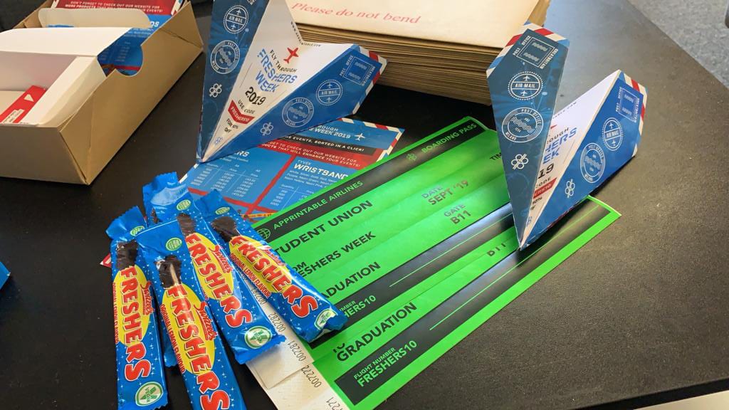 Green wristbands printed like boarding passes for a freshers week, with paper aeroplane flyers and sweets
